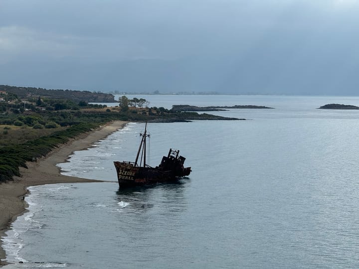Blick von oben auf ein verrostetes Schiffswrack im Wasser am Sandstrand.
